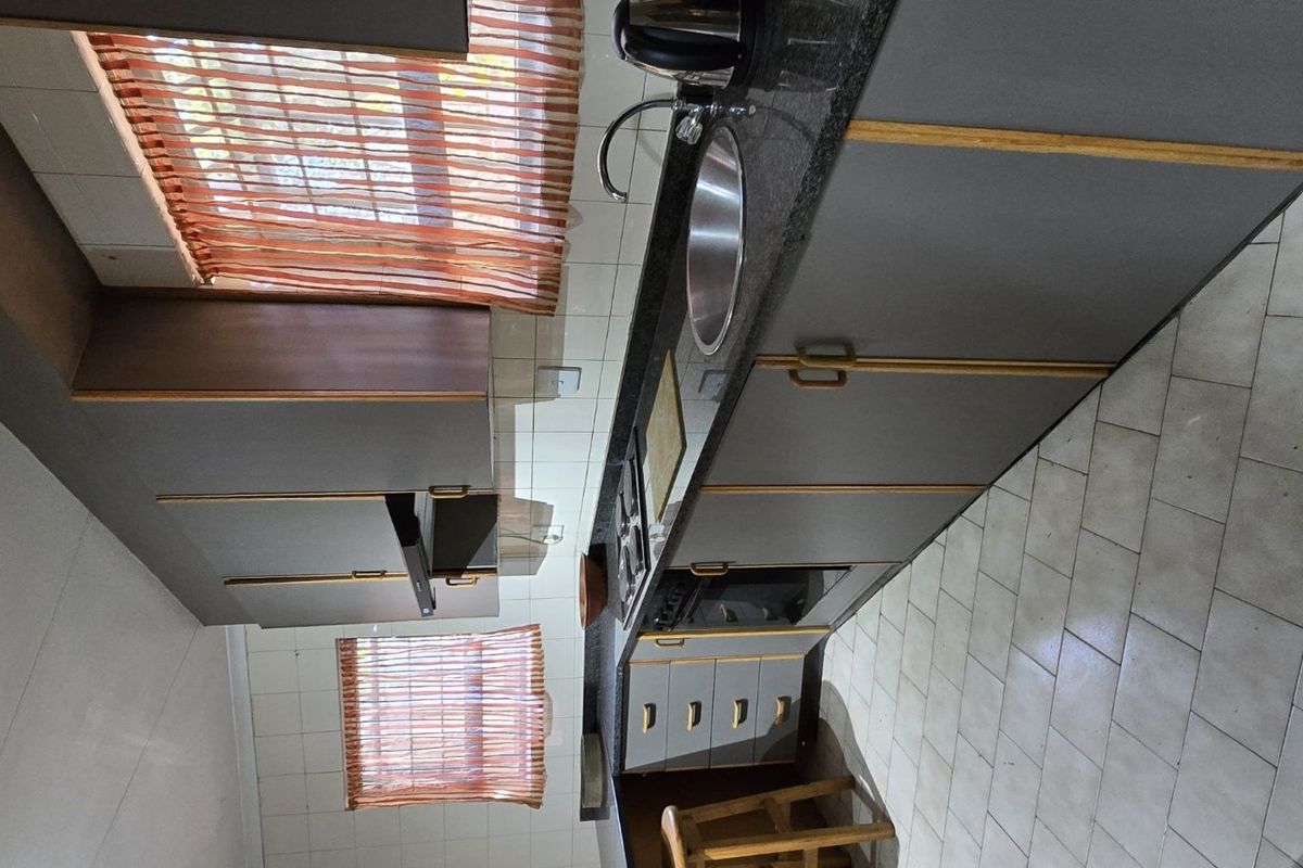 A functional kitchen featuring built-in cabinetry, laminate countertops, a stainless steel sink, and tiled flooring, offering a practical layout with potential for modern updates.
