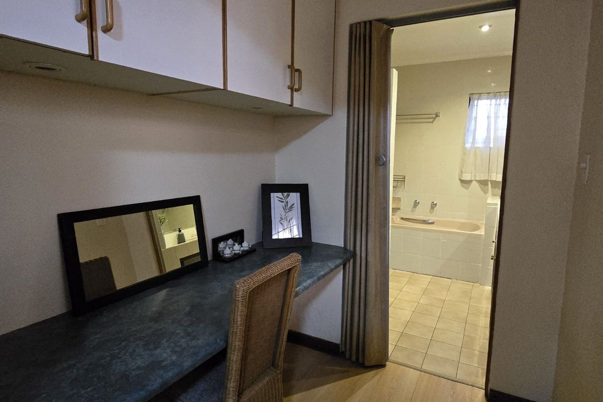 Bedroom featuring a built-in desk and overhead cabinetry, with a folding door providing direct access to an en-suite bathroom.