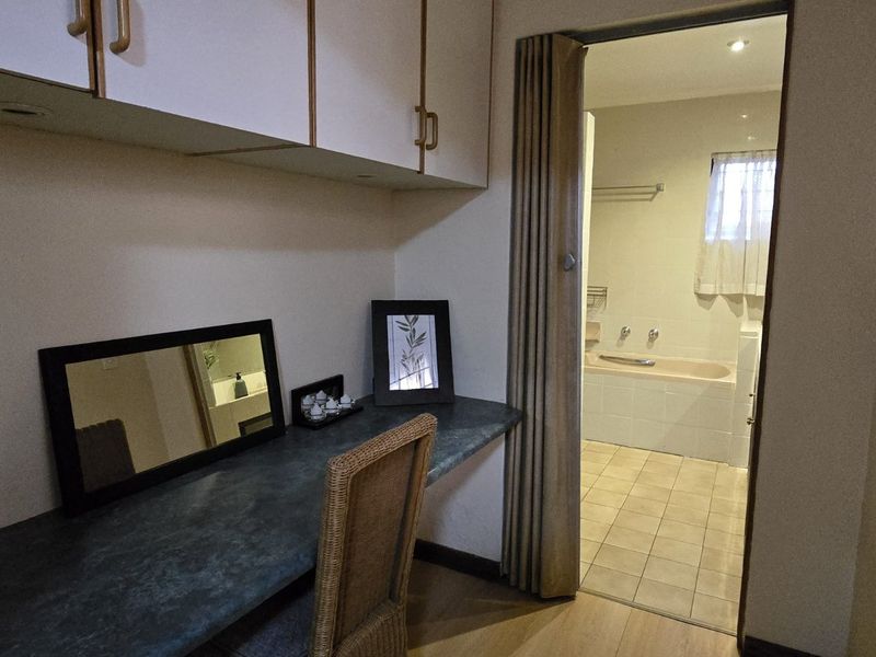 Bedroom featuring a built-in desk and overhead cabinetry, with a folding door providing direct access to an en-suite bathroom.