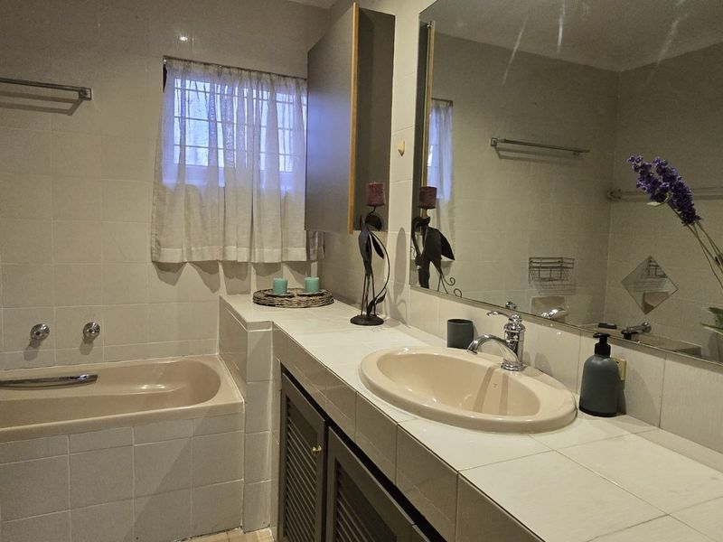 A functional bathroom featuring a built-in bathtub, tiled vanity countertop with integrated basin, and a large wall-mounted mirror.
