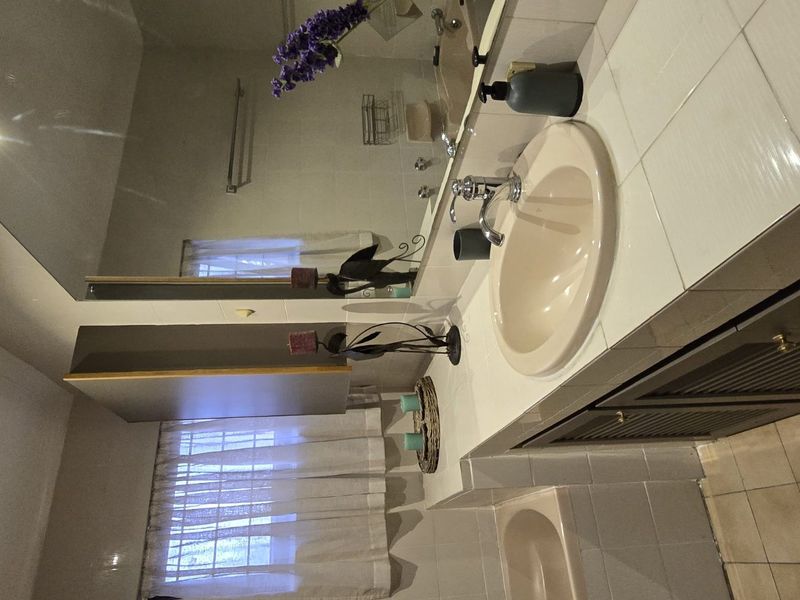 A functional bathroom featuring a tiled vanity with integrated basin, wall-mounted mirror, and tiled flooring, offering a dated aesthetic ready for modernization.