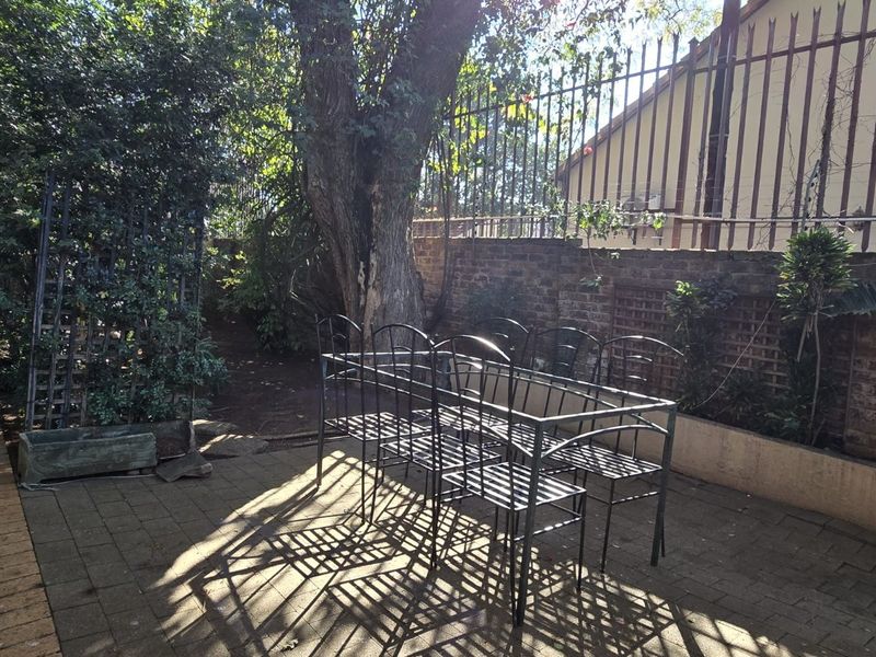 A private rear garden area featuring brick paving, established trees, and secure perimeter walling with metal fencing.