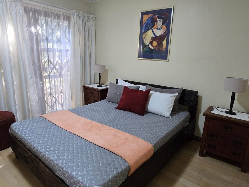 A well-lit bedroom featuring laminate flooring and a sliding glass door with an integrated security gate, providing access to the exterior.