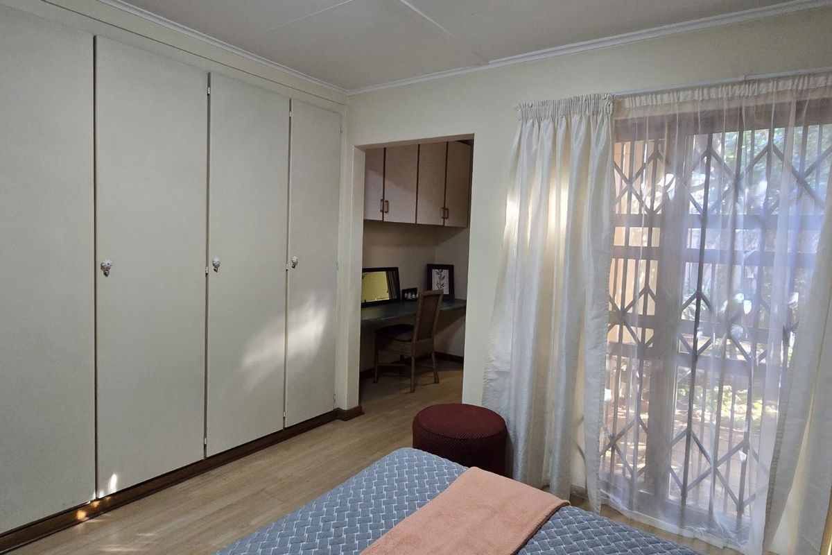 Bedroom featuring extensive built-in cupboards, a dedicated built-in desk area, and a sliding door with a security gate leading to the exterior.