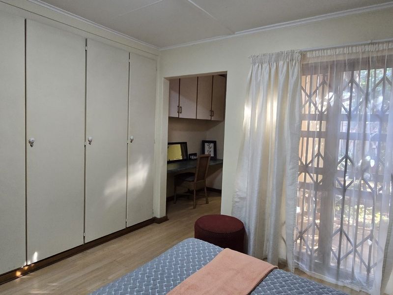 Bedroom featuring extensive built-in cupboards, a dedicated built-in desk area, and a sliding door with a security gate leading to the exterior.