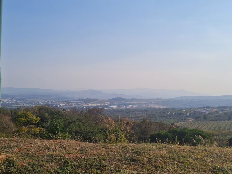 A wide-angle landscape view overlooking a valley with distant hills and agricultural land.