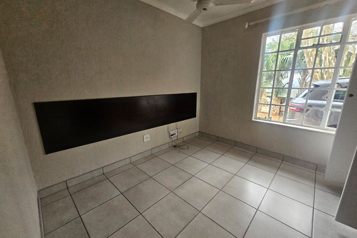 An empty bedroom featuring tiled flooring, a ceiling fan, and a built-in dark wood headboard, offering a neutral canvas for personalization.