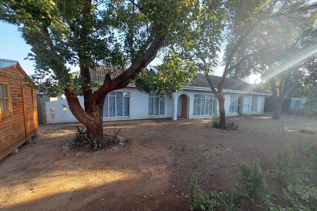 Rear view of the property featuring a white facade, tiled roof, security bars on windows, and a detached wooden shed in the garden area.