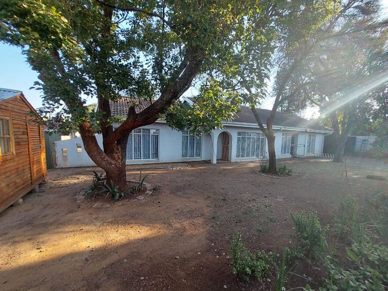 Rear view of the property featuring a white facade, tiled roof, security bars on windows, and a detached wooden shed in the garden area.