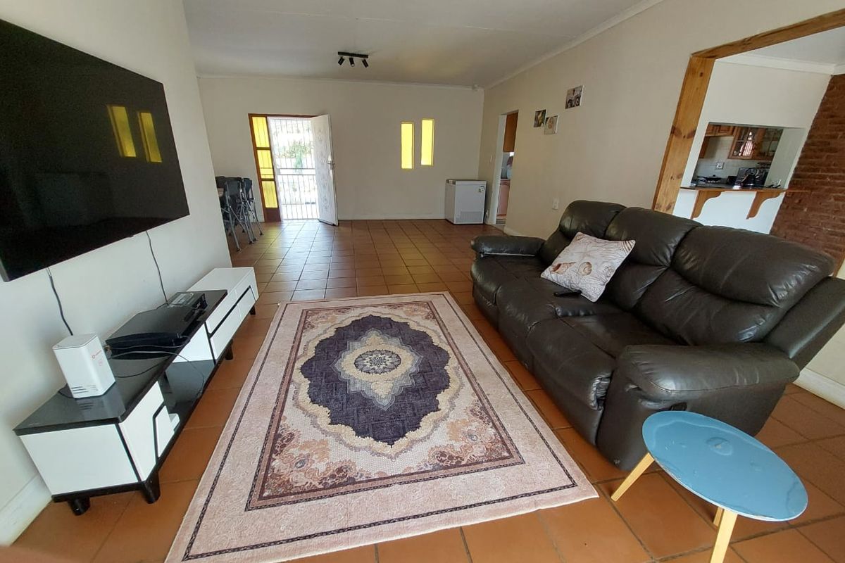 Spacious living area featuring terracotta-style tiled flooring, a pass-through window to the kitchen, and direct access to the front entrance.