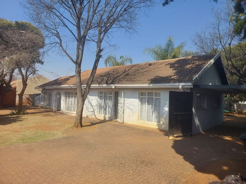 Front exterior view of a single-story house featuring a tiled roof, paved driveway, and security gates, showing signs of exterior wear.