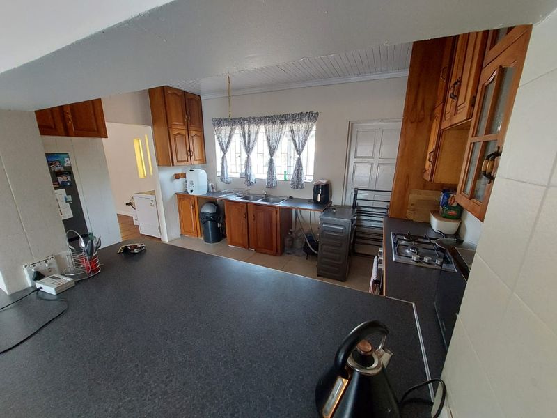 A functional kitchen featuring wooden cabinetry, laminate countertops, a gas hob, and a stainless steel sink, offering a practical layout with potential for modernization.