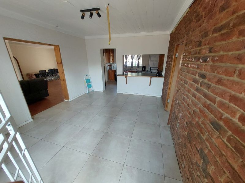 Open plan living area featuring large format floor tiles, an exposed brick feature wall, and a breakfast bar connecting to the kitchen space.