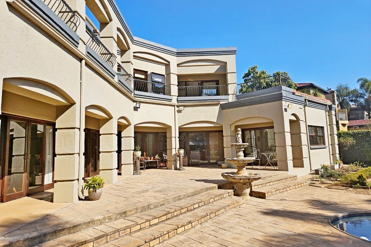Spacious rear patio featuring stone paving, a central fountain, and multi-level terrace access with arched architectural details and wrought iron balcony railings.