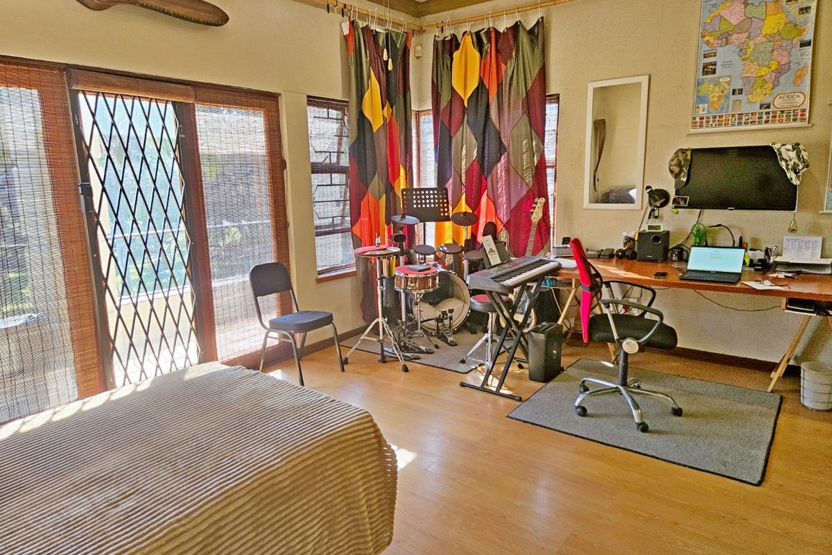 A bedroom featuring laminate flooring, large sliding glass doors with security gates, and natural light through louvre windows.