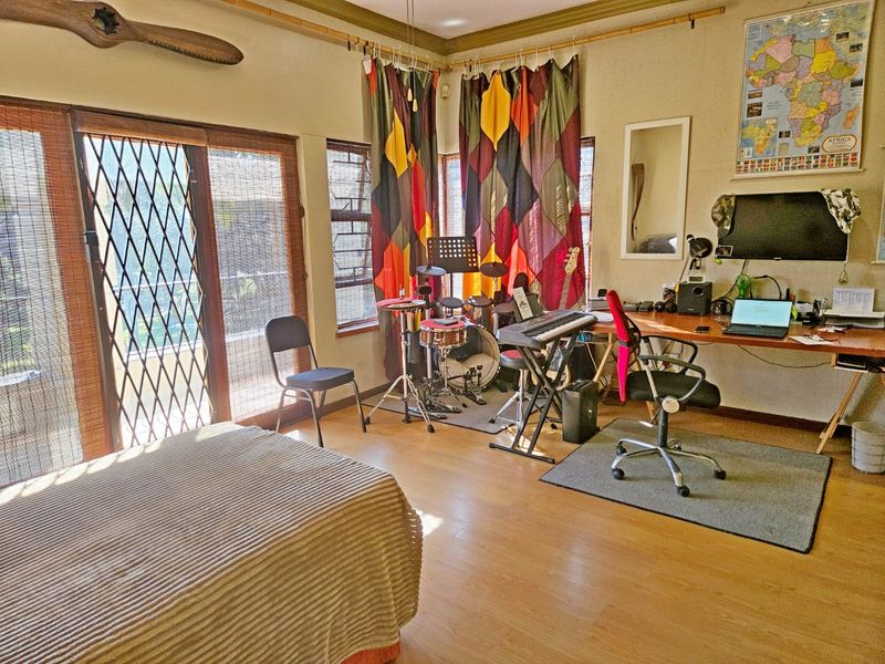 A bedroom featuring laminate flooring, large sliding glass doors with security gates, and natural light through louvre windows.