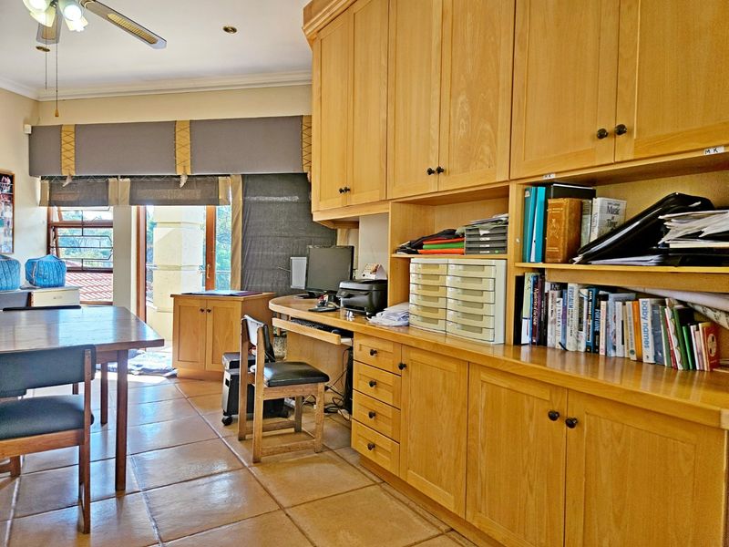 A home office featuring extensive built-in wooden cabinetry, tiled flooring, and direct access to an outdoor area through a sliding glass door.