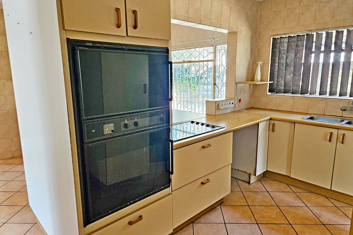 A dated kitchen featuring built-in oven, electric cooktop, laminate countertops, and ceramic tile finishes, offering potential for a modern renovation.