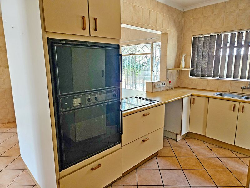 A dated kitchen featuring built-in oven, electric cooktop, laminate countertops, and ceramic tile finishes, offering potential for a modern renovation.