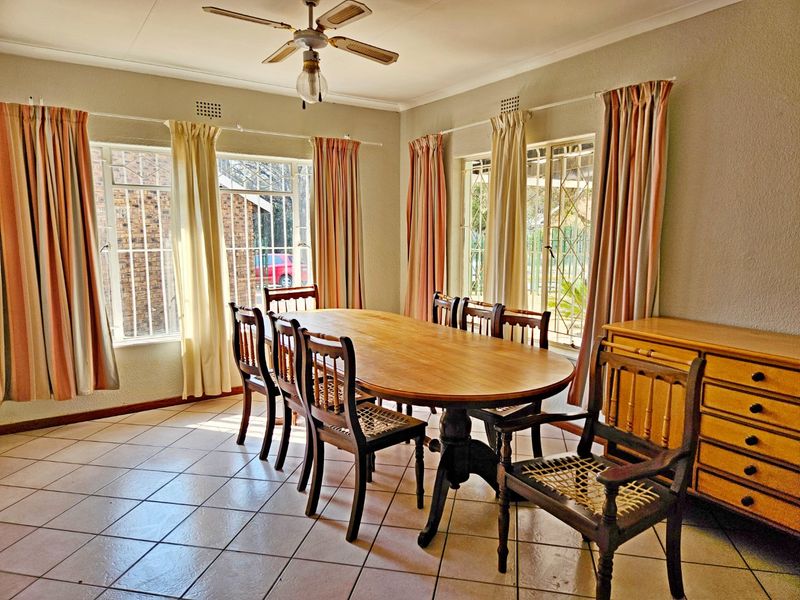 A dining room featuring tiled flooring, a ceiling fan, and large windows with security bars, providing a functional space for family meals.