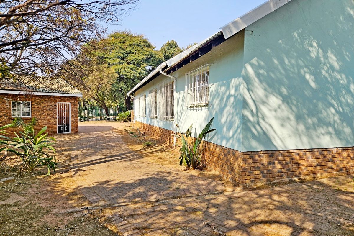 A view of the rear exterior of the house featuring brick paving, security bars on windows, and a combination of brick and plastered wall finishes.