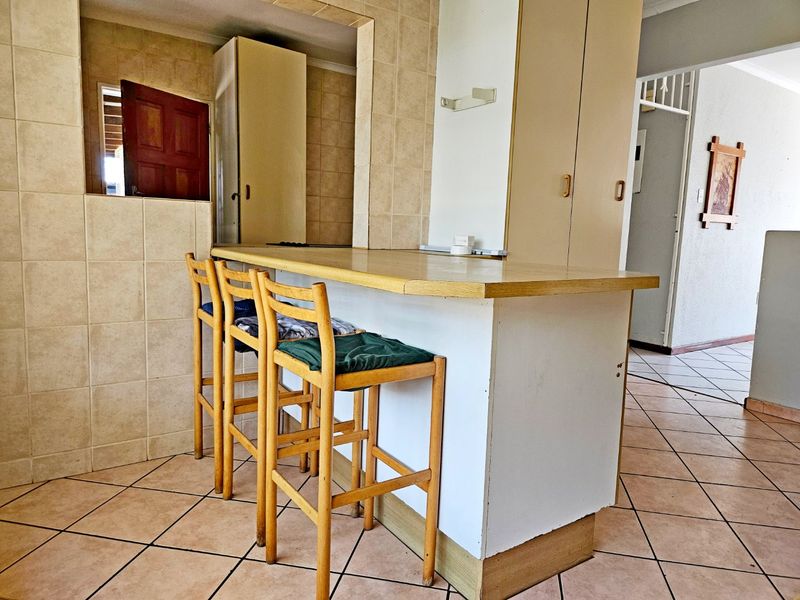 A functional kitchen area featuring a breakfast bar, tiled splashbacks, and built-in cabinetry with ceramic floor tiles throughout.