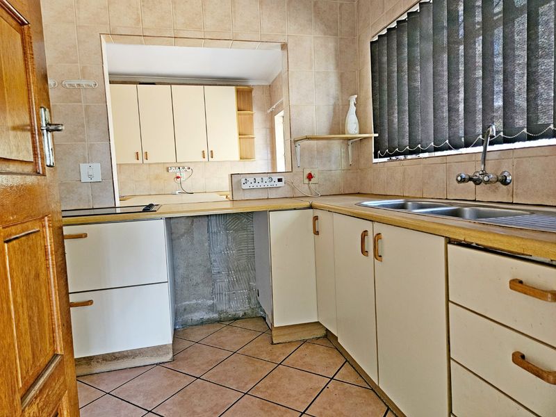 A dated kitchen featuring built-in cabinetry, laminate countertops, and a stainless steel sink, requiring cosmetic updates and repairs to the cabinetry and wall finishes.