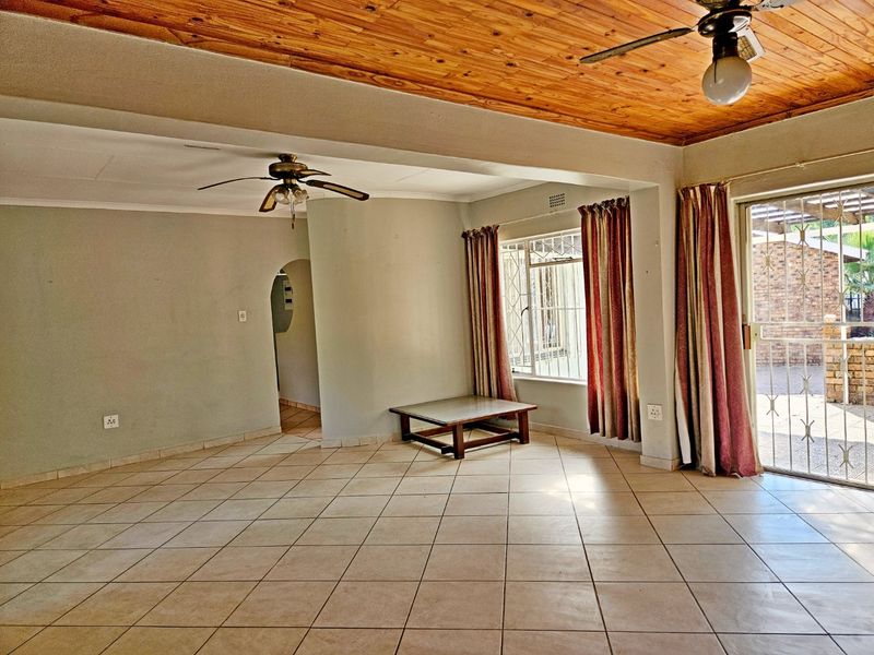 Spacious living area featuring tiled flooring, a timber ceiling, ceiling fans, and direct access to the outdoor area through a security gate.