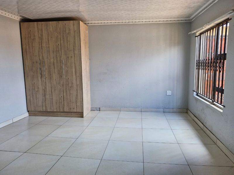 A simple, empty bedroom featuring tiled flooring, a built-in wooden wardrobe, and security bars on the window.