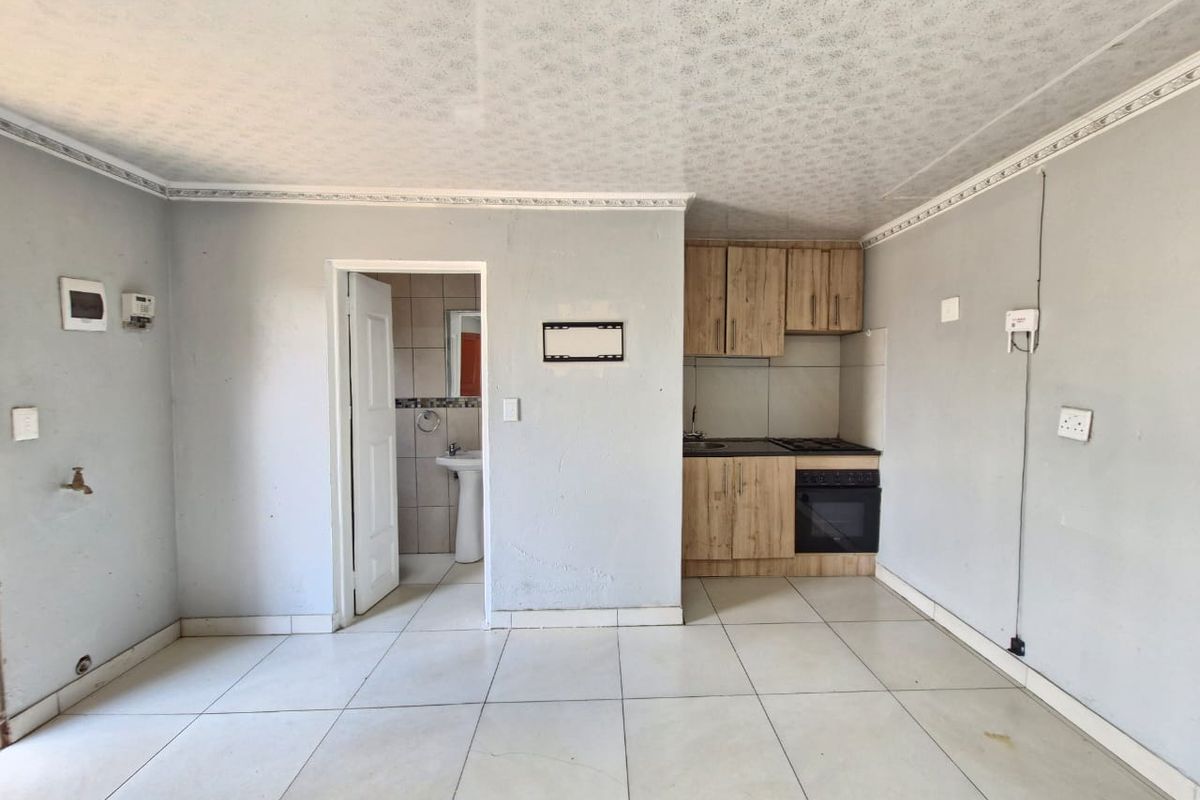 Open plan living area featuring a compact kitchenette with built-in cabinetry and oven, adjacent to a small bathroom with a pedestal basin.