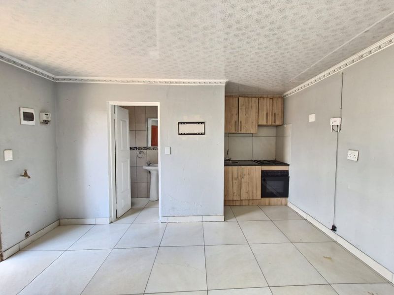 Open plan living area featuring a compact kitchenette with built-in cabinetry and oven, adjacent to a small bathroom with a pedestal basin.