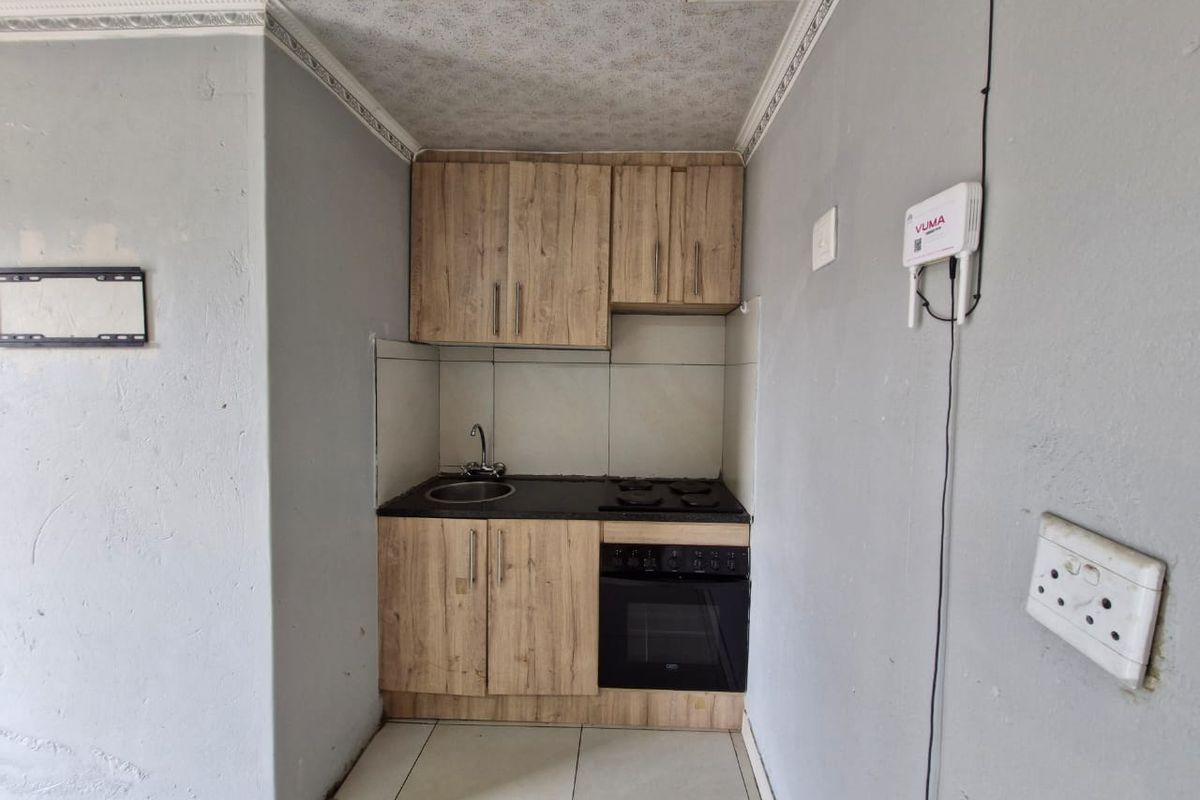 Compact kitchen featuring wood-look cabinetry, built-in oven and hob, tiled backsplash, and neutral floor tiles.