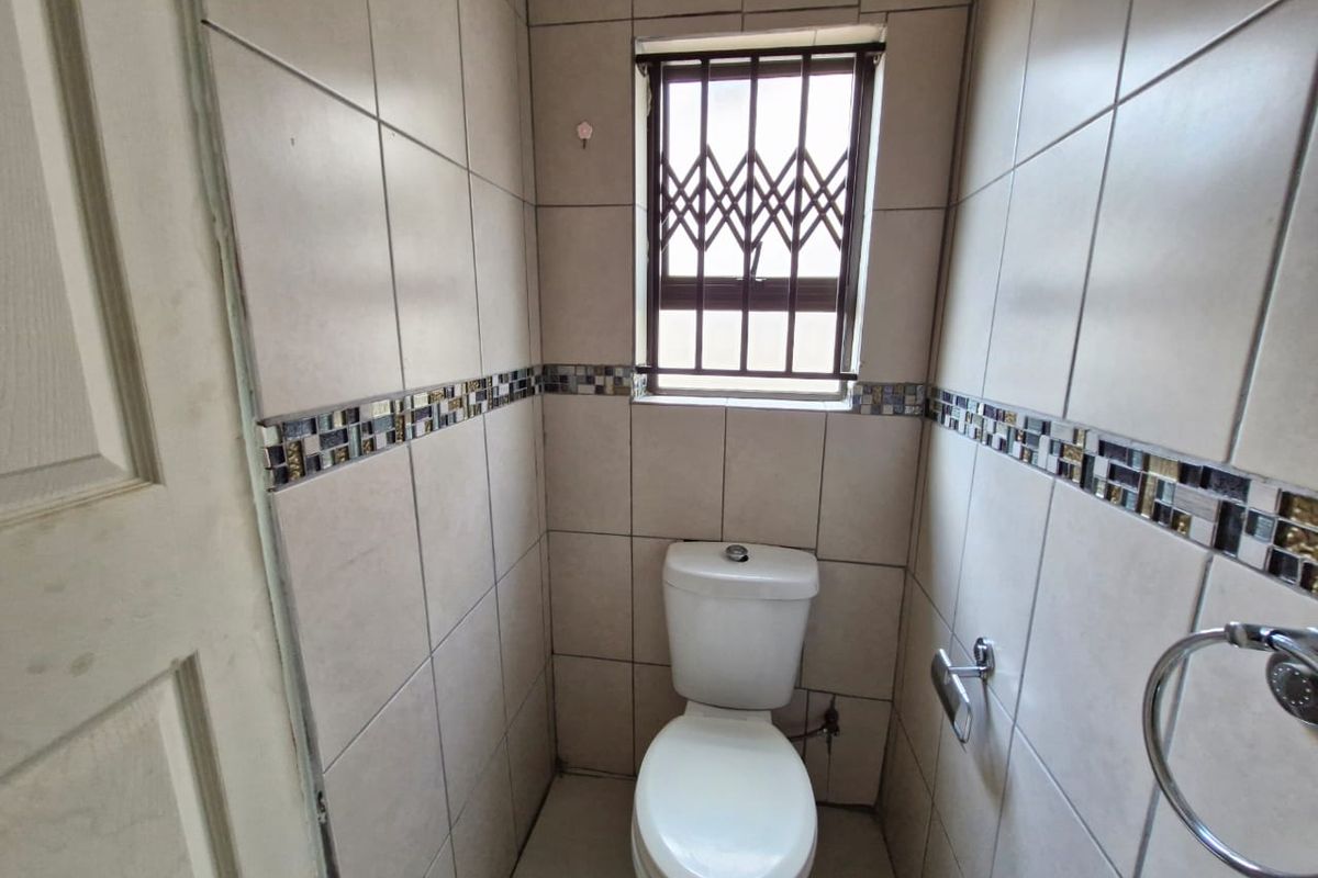 A compact, fully tiled guest bathroom featuring a standard toilet, mosaic tile accents, and a window with a security gate.