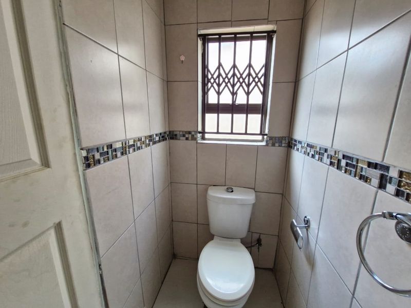 A compact, fully tiled guest bathroom featuring a standard toilet, mosaic tile accents, and a window with a security gate.