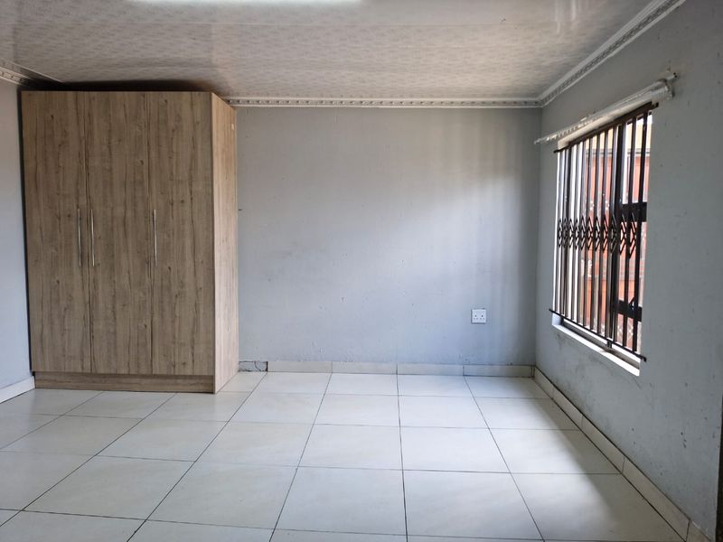 A simple bedroom featuring tiled flooring, a built-in wardrobe, and security bars on the window.