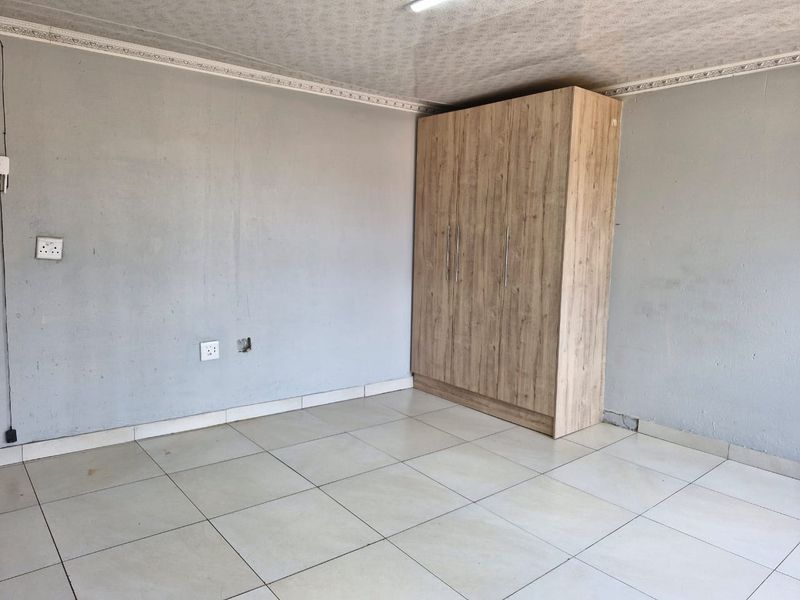 A bedroom featuring tiled flooring, a built-in wooden wardrobe, and ceiling cornice detailing. The space is vacant and ready for personalization.