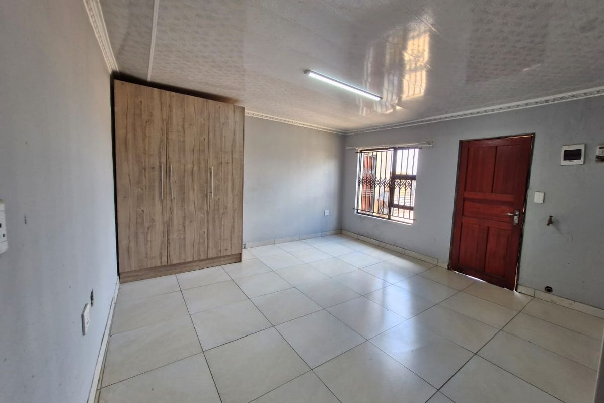 A clean, empty bedroom featuring tiled flooring, a built-in wardrobe, and a window with a security gate.
