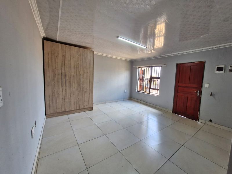 A clean, empty bedroom featuring tiled flooring, a built-in wardrobe, and a window with a security gate.