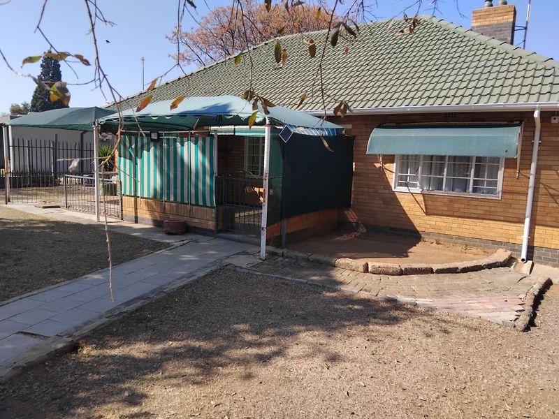 Rear view of a brick house featuring a tiled roof, paved pathways, and window security bars, set within a garden area.