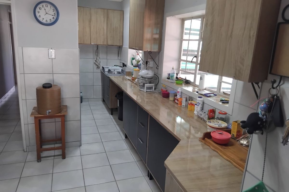A functional kitchen featuring built-in cabinetry, laminate countertops, tiled flooring, and a tiled backsplash, providing a practical workspace with natural light.