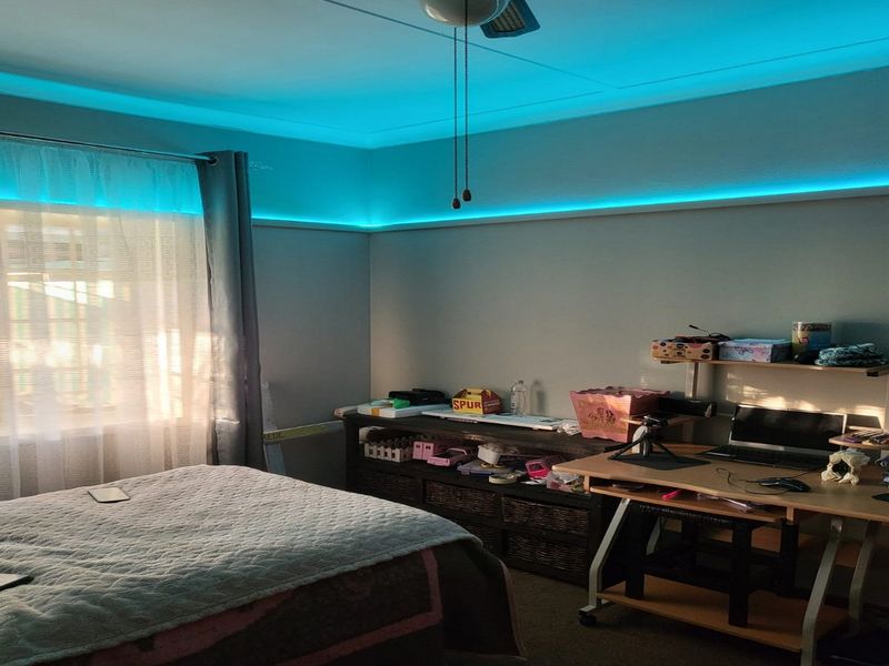 A bedroom featuring blue cove lighting and a ceiling fan, providing a functional space with natural light from the window.