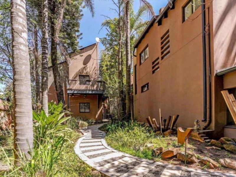 A landscaped rear garden featuring a paved pathway winding between multi-story residential structures with mature trees and established greenery.