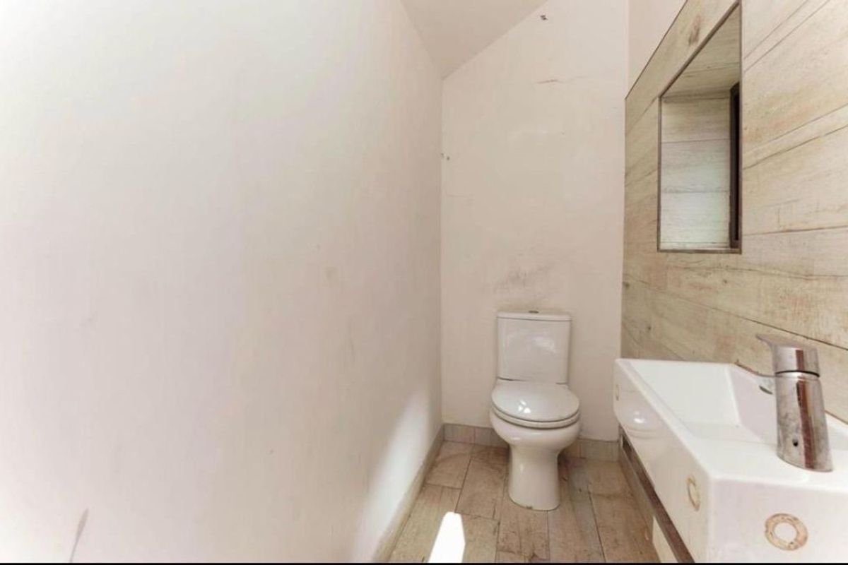 A compact bathroom featuring a toilet, wall-mounted washbasin with faucet, and a tiled accent wall with a mirror.