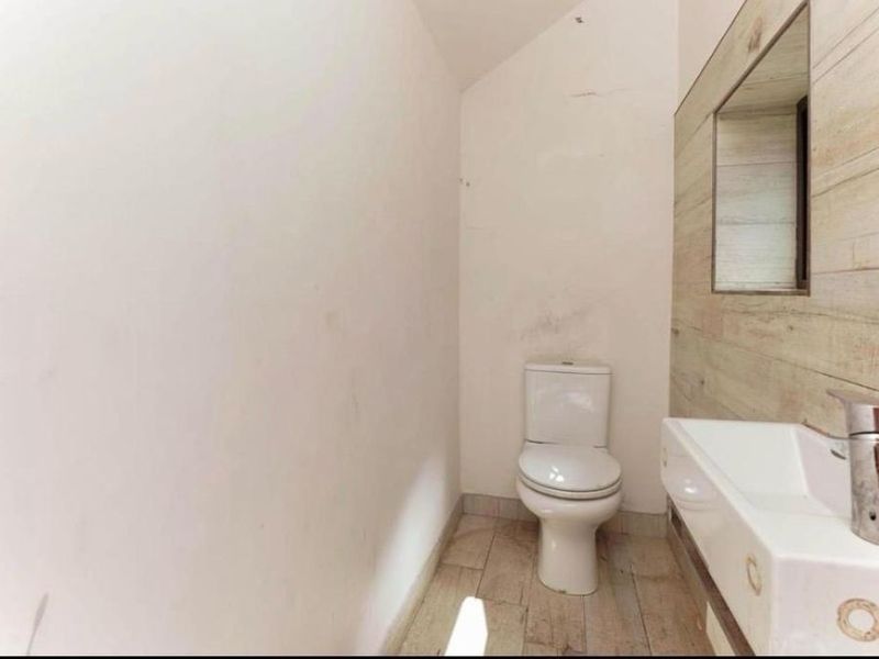 A compact bathroom featuring a toilet, wall-mounted washbasin with faucet, and a tiled accent wall with a mirror.