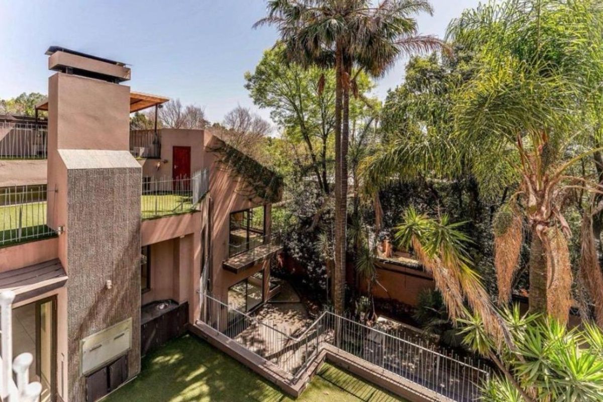 A multi-level rear exterior view featuring a built-in fireplace, terraced balconies with metal railings, and mature garden landscaping.