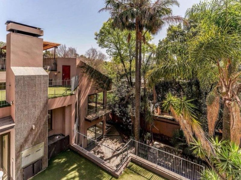 A multi-level rear exterior view featuring a built-in fireplace, terraced balconies with metal railings, and mature garden landscaping.