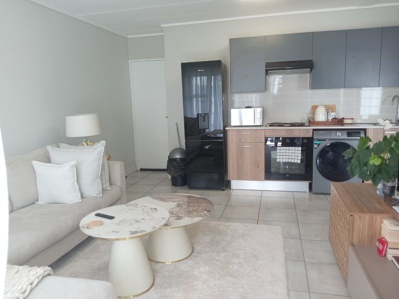 Open-plan living area featuring a modern kitchen with built-in cabinetry, oven, hob, and extractor fan, seamlessly connected to the lounge space with tiled flooring.
