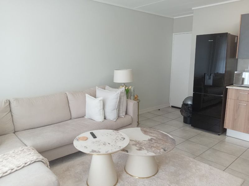 Open plan living area featuring neutral wall tones and tiled flooring, seamlessly connecting to a compact kitchen space.