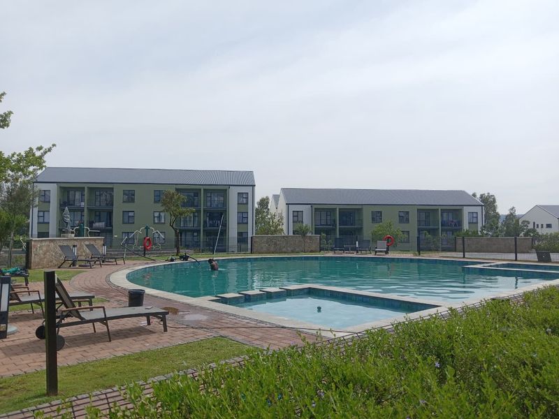 Communal swimming pool area featuring a paved deck, landscaped surroundings, and views of the multi-story apartment complex buildings.