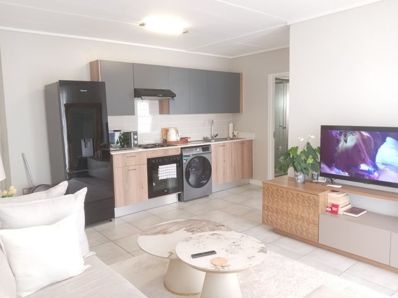 Modern open-plan living area featuring a compact kitchen with built-in cabinetry, integrated appliances, and neutral tiled flooring throughout the combined space.
